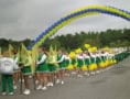 A parade of cheerleaders and a high school band pass under an arch of blue and yellow balloons