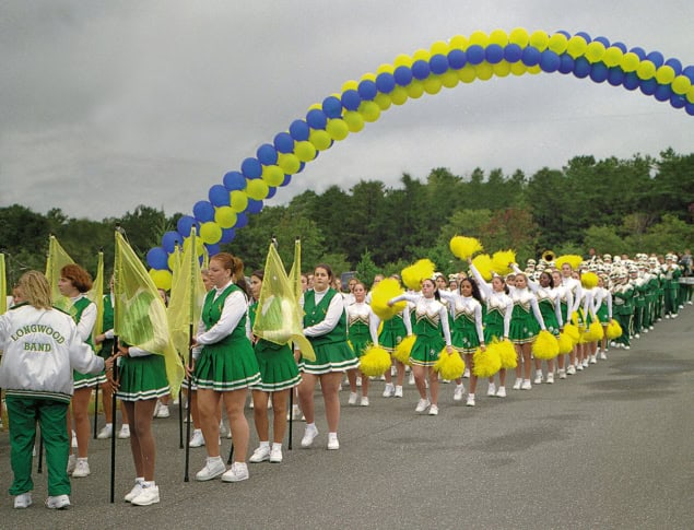 A parade of cheerleaders and a high school band pass under an arch of blue and yellow balloons A parade of cheerleaders and a high school band pass under an arch of blue and yellow balloons