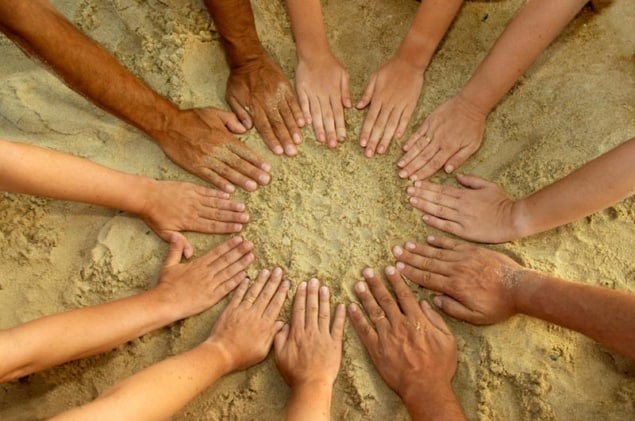 Photo of 12 hands forming a circle on a beach