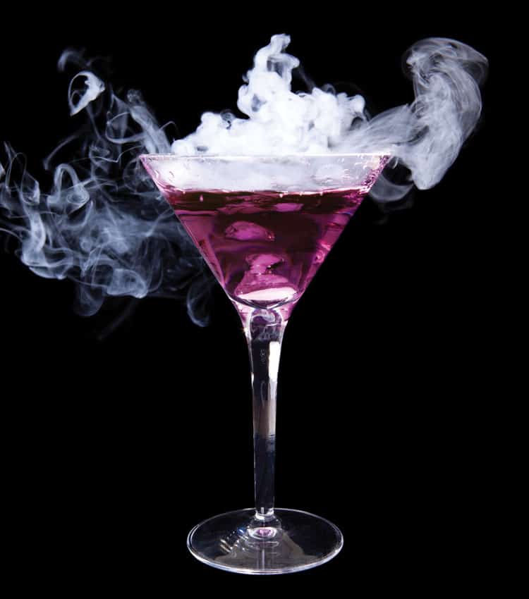 Cocktail glass containing a purple liquid, which is emitting dramatic white, smoky wisps