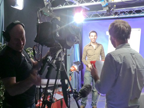 Camera operator with a video camera on a tripod, a man stood in a spotlight and a man with a clipboard Camera operator with a video camera on a tripod, a man stood in a spotlight and a man with a clipboard
