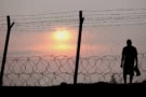 Man standing behind a barbed wire fence at sunset