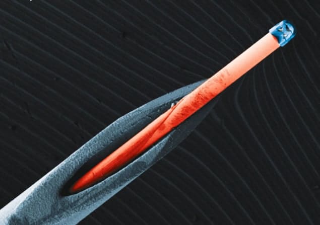 Coloured electron microscope image of a miniaturized triplet lens mounted on the end of an optical fibre