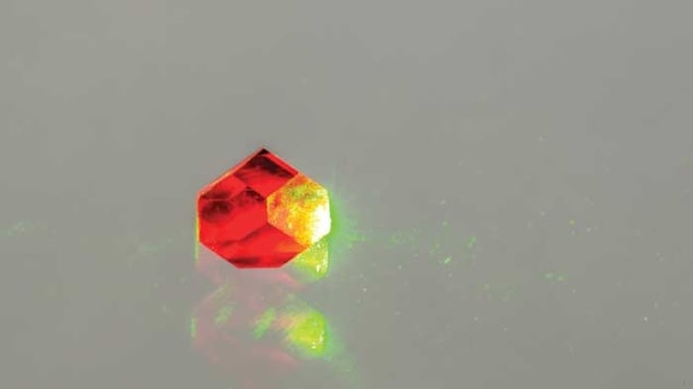 A photo of a reddish-coloured diamond with NV centres being illuminated with a green-yellow laser beam