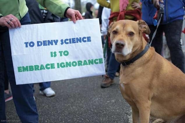 Photograph of a dog next to a sign saying &ldquo;To deny science is to embrace ignorance&rdquo; at a science march at Stony Brook University in April 2017