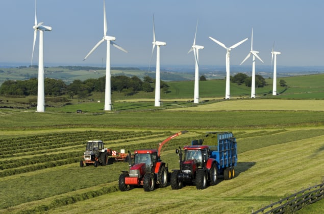 Photo of farmer collecting silage in front of wind turbines. Courtesy: iStock/Stephen Meese