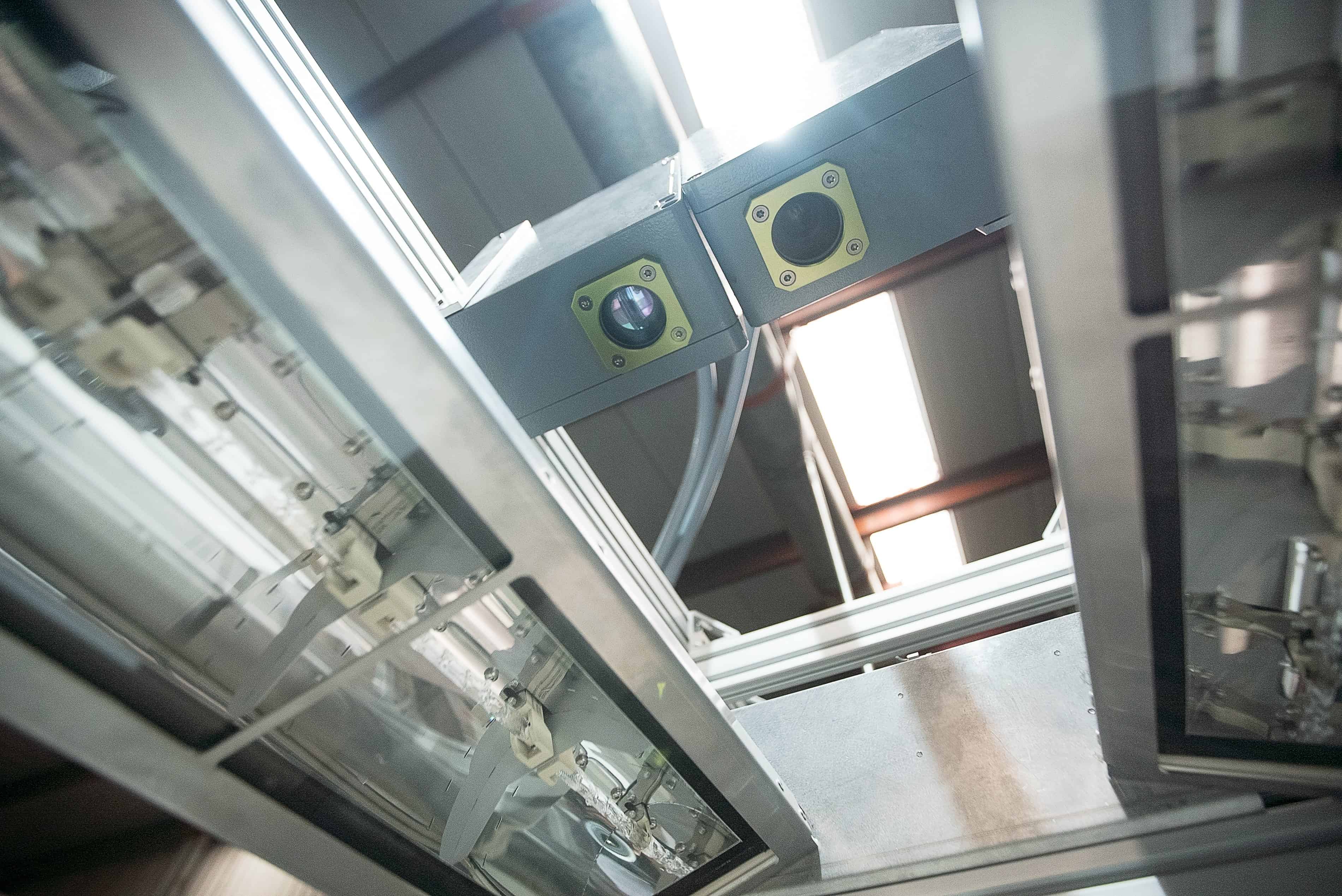 Photo showing two cameras suspended on a metal frame above a production line in a factory