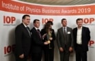 A group of five people standing beneath a banner reading "Institute of Physics Business Awards 2019" and holding a rectangular-prism-shaped award