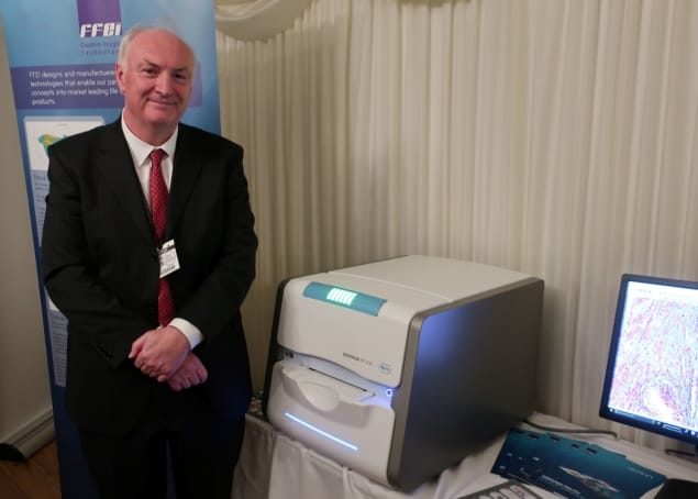 Photo of a man in a business suit, Martin Gouch, standing next to a scanner and a computer screen displaying an image of a tissue biopsy