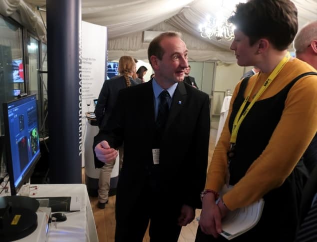 A man in a business suit talking with a woman in a bright yellow turtleneck and pointing to an image on a computer screen