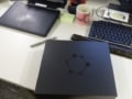 A photo of a black box decorated with a symbolic carbon ring, sitting on a desk next to a keyboard, laptop, pen and coffee cup