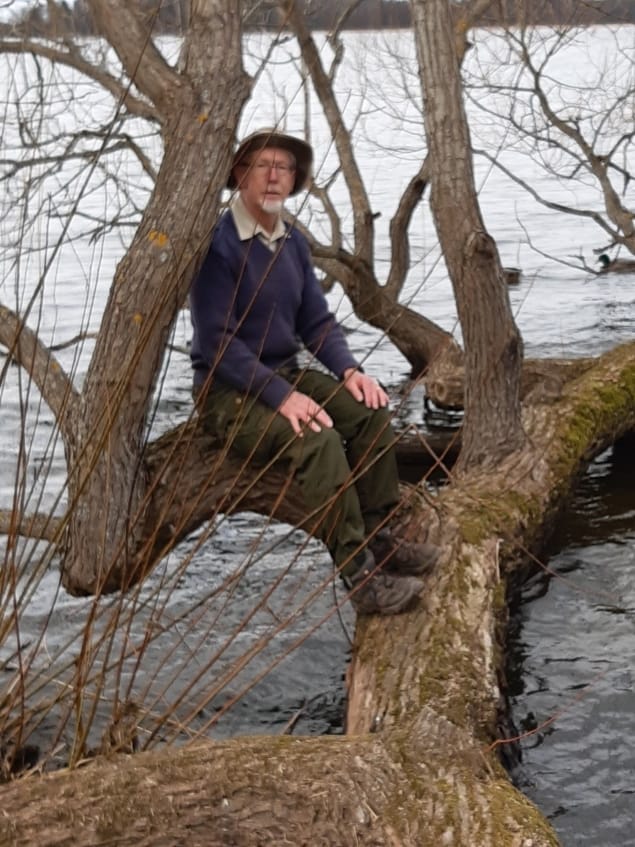 Steven Savage sitting on the branch of a tree bent over a lake