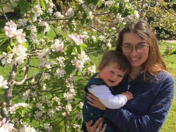 Rose Waugh holds her baby son while standing in front of a blossoming tree