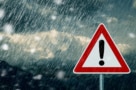 Photo of a triangular warning sign with a red border and a black exclamation mark, against a background of stormy skies