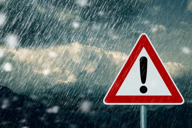 Photo of a triangular warning sign with a red border and a black exclamation mark, against a background of stormy skies