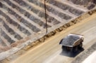 A photo of a truck carrying a load of ore-bearing rock past the stepped surface of an open-pit copper mine