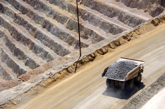 A photo of a truck carrying a load of ore-bearing rock past the stepped surface of an open-pit copper mine