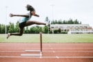 woman jumping a hurdle on athletic track