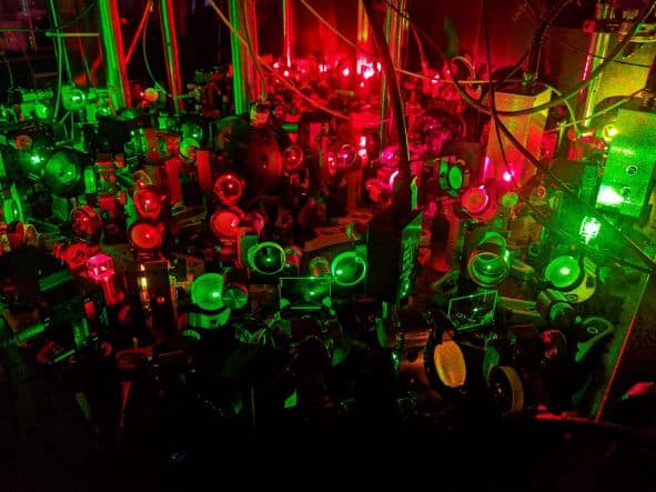 Photo of the optical setup used in the experiment, showing various optics bathed in green and red light