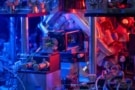 Fotografija vakuumske komore, optičnih vlaken in drugih komponent, obsijanih z modro in rdečo svetlobo