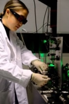 Photo of Helen Zeng in an optics lab wearing protective eyewear as she adjusts optics on a bench