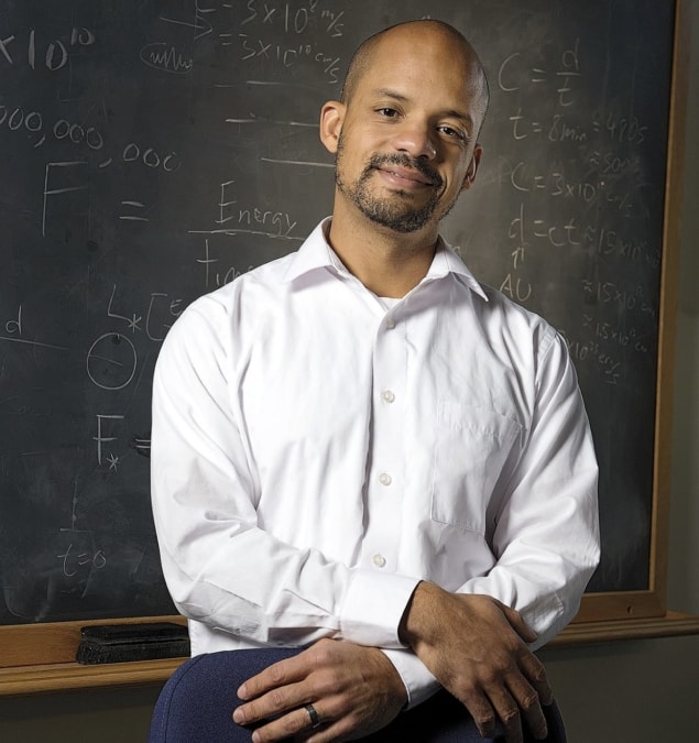 Photo of John Johnson standing in front of a blackboard covered in equations and mathematical symbols