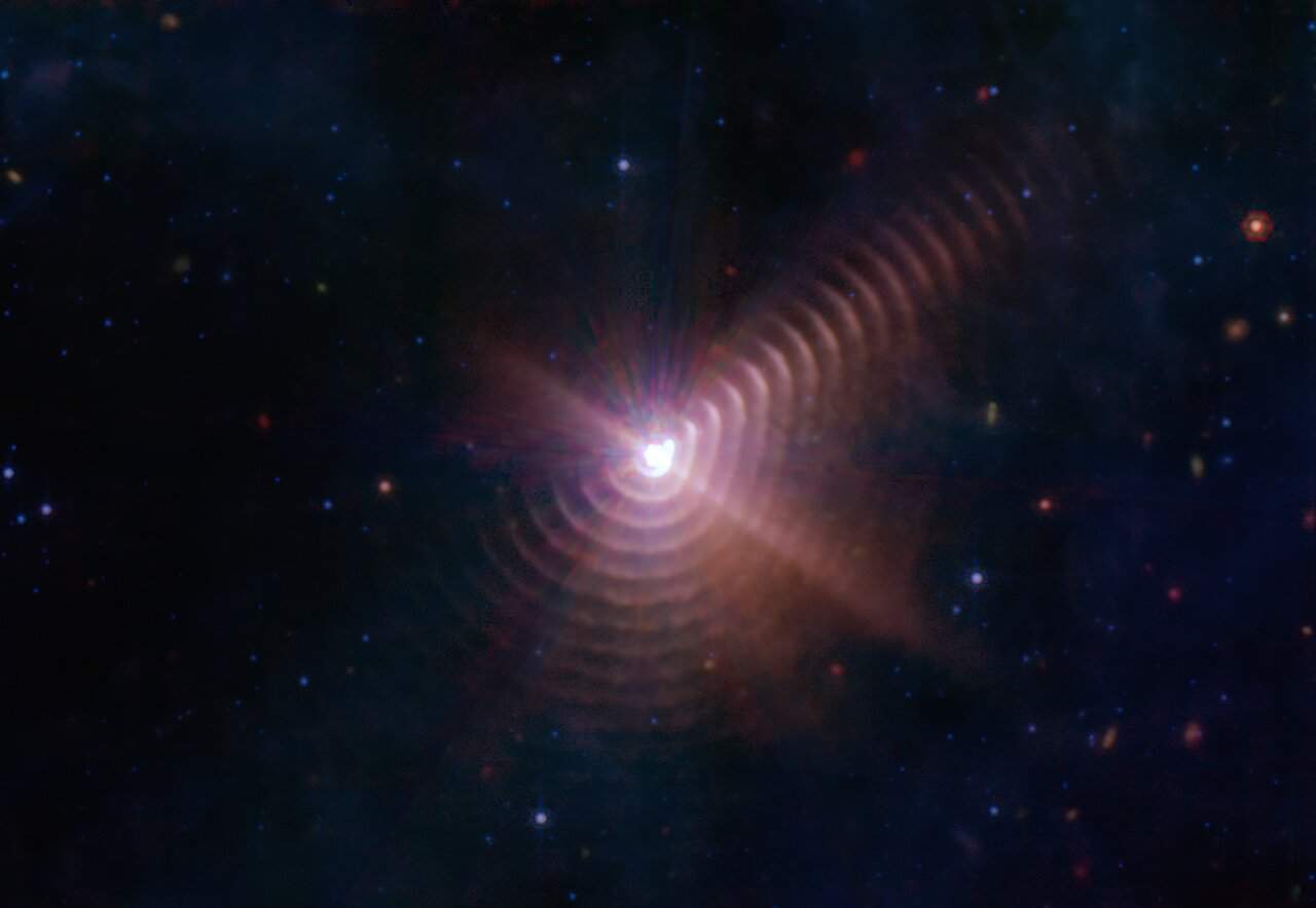 Image of the star WR 140, which appears as a burst of purplish light at the centre, surrounded by thin rings like water ripples in a pond