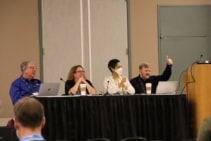 Fotografia de Bill Thigpen, Jennifer Ott, Chyree Batton e Mark Fernandez, sentados atrás de uma mesa durante o painel de discussão. Fernandez está fazendo um sinal de positivo