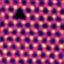 A filtered and coloured scanning transmission electron microscopy image showing a vacancy in a lattice of hexagonal boron nitride. The vacancy appears as a triangular dark spot in a brightly glowing lattice of atoms