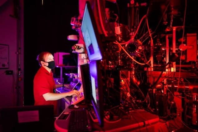 Photo of Ryan Schoell looking at a computer screen in a dark laboratory bathed in red laser light