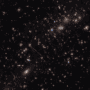 Image of many galaxies on a dark background. Two of the most prominent features in the image include the Thin One, located just below and left of the image center, and the Fishhook, a red swoosh at upper right.