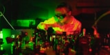 A photo of a researcher, Bereneice Sephton, wearing protective goggles and manipulating a component on an optical bench