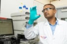 Photo of Vivek Kumar in a lab coat, safety goggles and gloves holding a glass vial containing the hydrogel