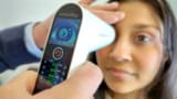 Hands holding a small piece of medical equipment in front of a patient's eye