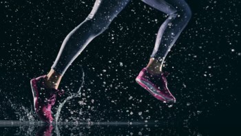 The pink trainers of a runner splashing through water against a black background