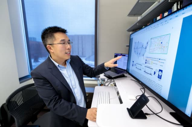 Photo of Liang Jiang in an office pointing at a computer screen displaying a map of the proposed quantum network