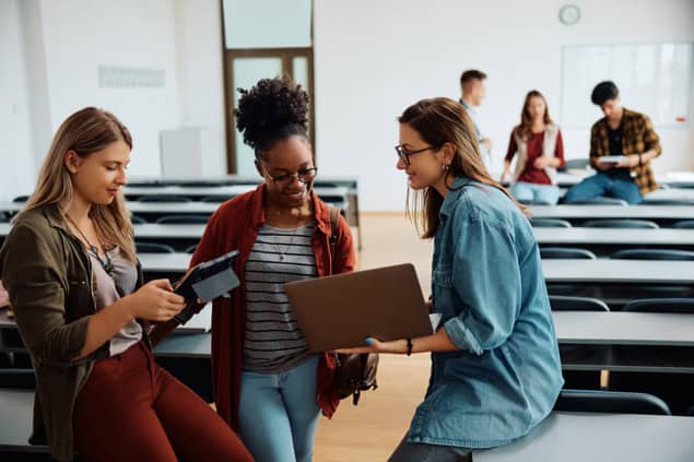 Multiracial group of female students using wireless technology in university classroom