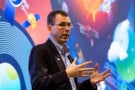 Photo of Chris White-Horne giving a conference talk. In the background is a slide displaying a colourful image of satellites, planets and stars