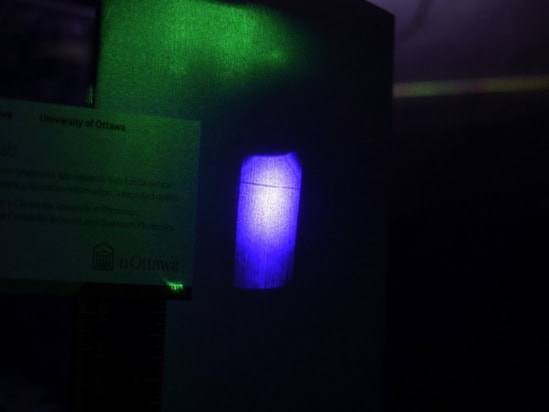 Photo of the laser shadow in a dark laboratory, where it appears as a faint black line across a bright blue background