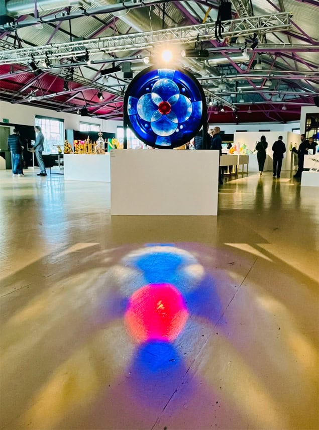 A glass artwork in a large gallery space with light shining through and reflecting colours on the floor