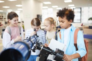 Group of four curious children using modern school telescope to look at sky, horizontal shot