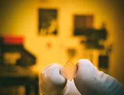 Photo of a chip made of the non-crystalline topological semimetal niobium phosphide, which appears as a light-orange square held in a person's gloved hands