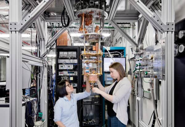 Two women scientists working on a quantum computer suspended from a large metal frame