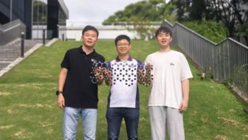 Photo of the three NUS researchers who were part of the multidisciplinary research team that developed the Janus graphene nanoribbons. They're standing on a grassy slope and holding a model of a nanoribbon