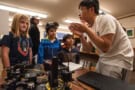 Group of children listening to an adult explaining some examples of technology on the table between them