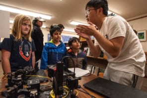 Group of children listening to an adult explaining some examples of technology on the table between them