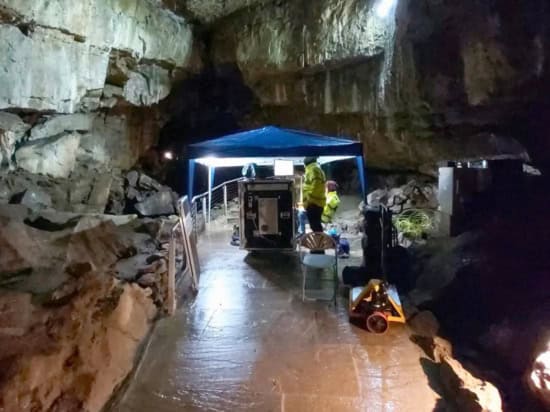 Two people in hi-vis with a large metal object in an underground cavern