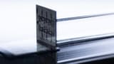 Photo of the Ocelot quantum computer chip, a grey and black square with circuits etched into it, shown standing on its edge