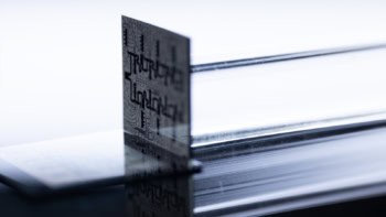 Photo of the Ocelot quantum computer chip, a grey and black square with circuits etched into it, shown standing on its edge
