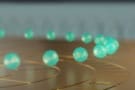 In this artist's depiction of a trapped-ion quantum computer, green, triangular-faceted blobs hover in a ring above a gold surface divided into compartments